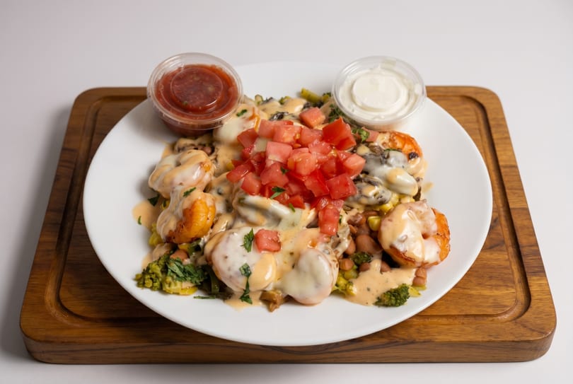 Shrimp and oysters covered in cheese sauce, diced tomatoes, with salsa and sour cream on the side.